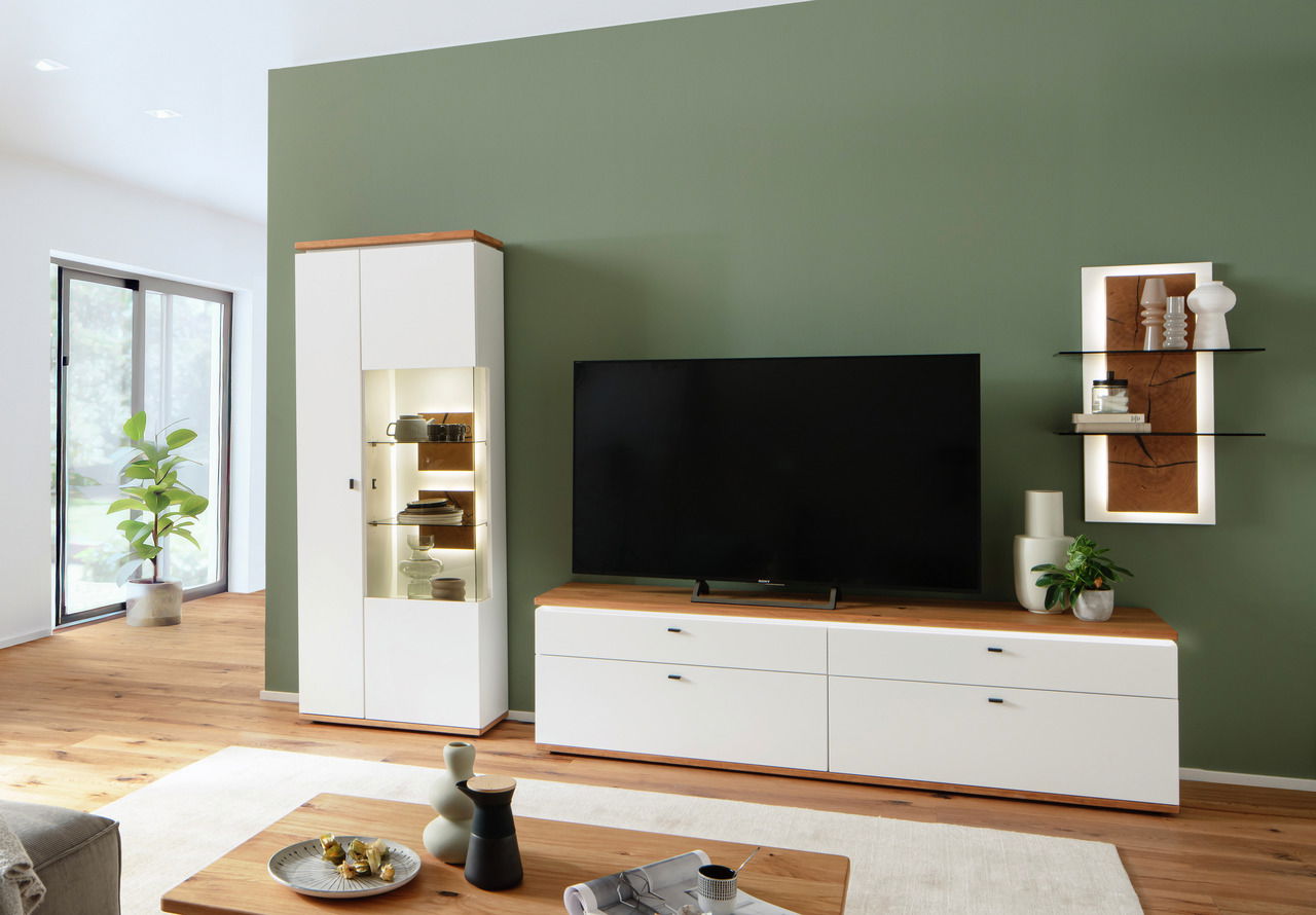 Moderne Wandkombination in Weiß mit Holzakzenten, bestehend aus einem hohen Schrank mit Glaseinsätzen, einem breiten TV-Schrank und einem dekorativen Wandregal, frontal betrachtet.