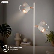 Weiße Stehleuchte mit vier schwenkbaren, geriffelten Spot-Köpfen und kupferfarbenen Akzenten, seitliche Perspektive vor grauer Wand im Wohnraum