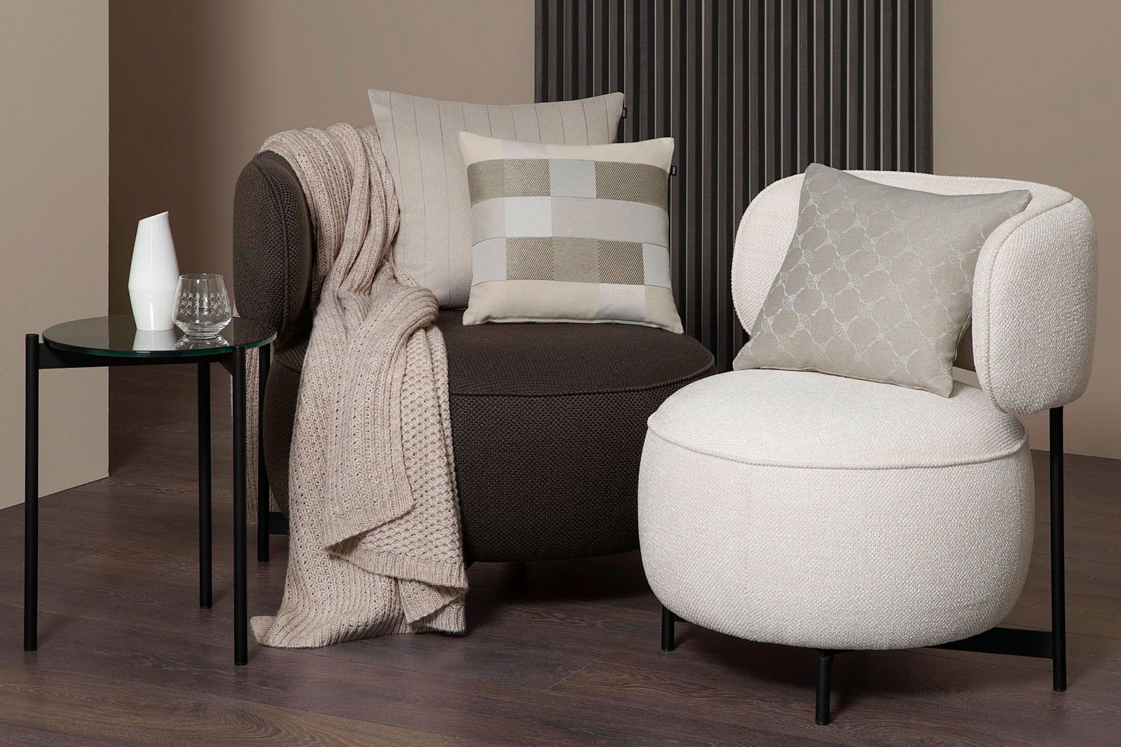 JOOP! Zierkissenhülle J!RIBBON Zwei moderne Sessel mit dekorativen Kissen in einem stilvollen Wohnzimmer. Der linke Sessel ist dunkelbraun mit einem beigen Strickplaid und einem karierten Kissen. Der rechte Sessel ist cremefarben mit einem gemusterten Kissen. Perspektive: Frontalansich
