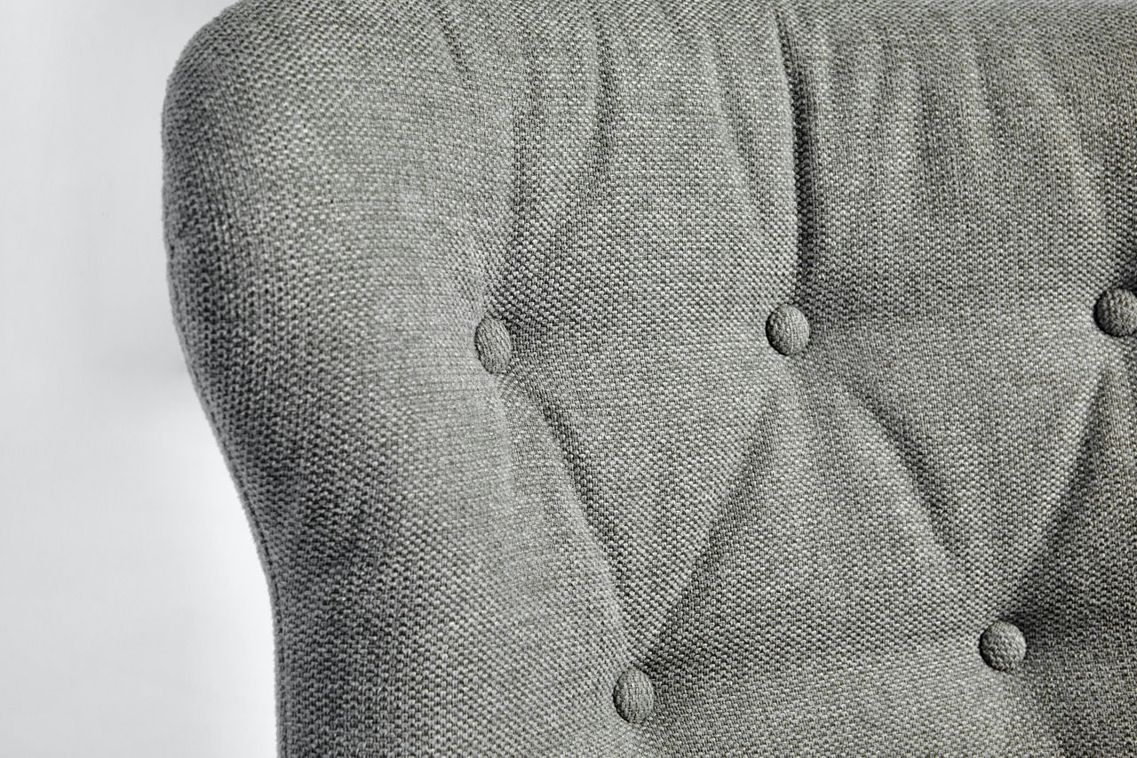 Nahaufnahme der Rückenlehne eines grauen, gepolsterten Stuhls mit Knopfdetails.