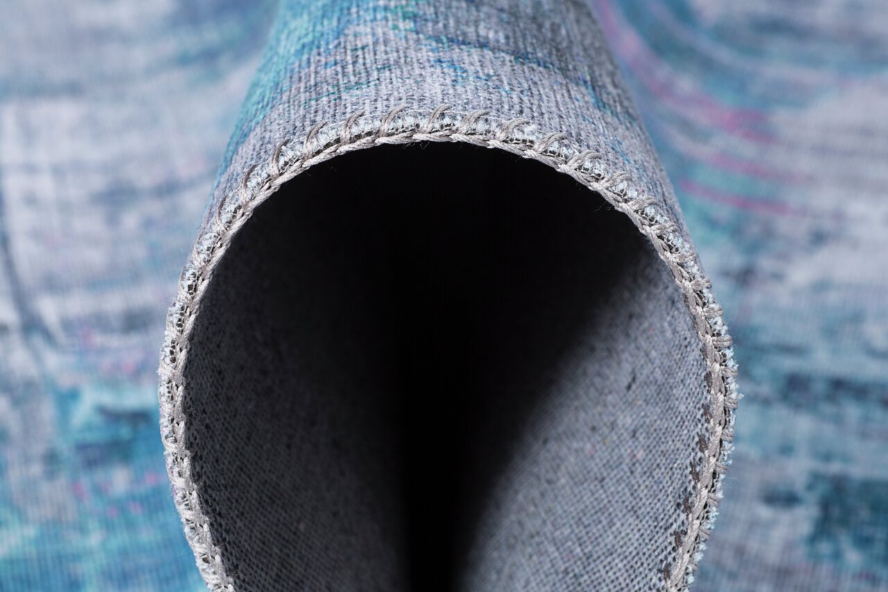 Nahaufnahme eines aufgerollten Teppichs mit sichtbarer Kante und blauen Mustern.