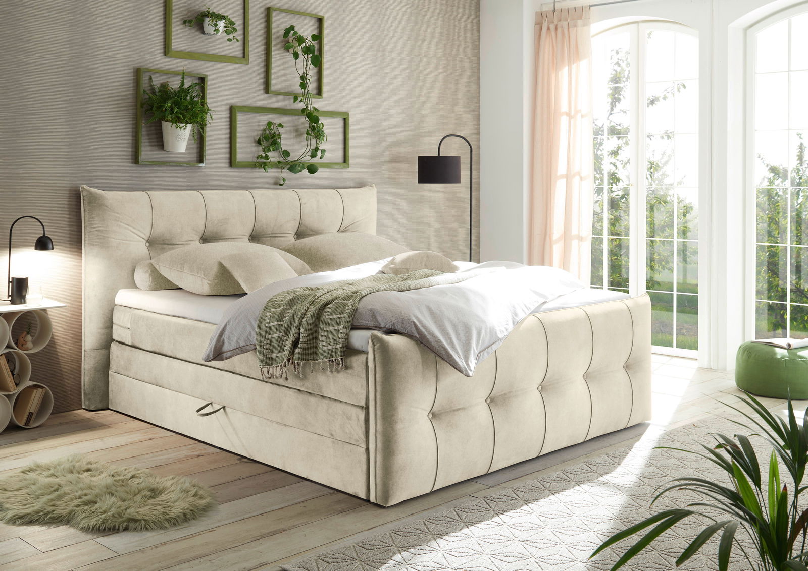 Boxspringbett in einem hellen Schlafzimmer mit großen Fenstern, Pflanzen und moderner Dekoration, seitliche Perspektive