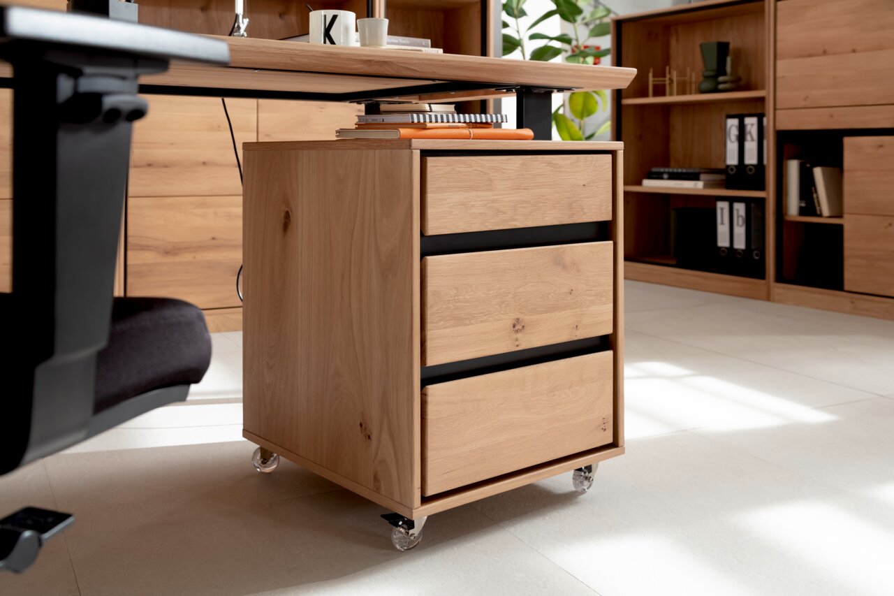 Rollcontainer aus Holz mit drei Schubladen, auf Rollen, seitliche Perspektive unter einem Schreibtisch.