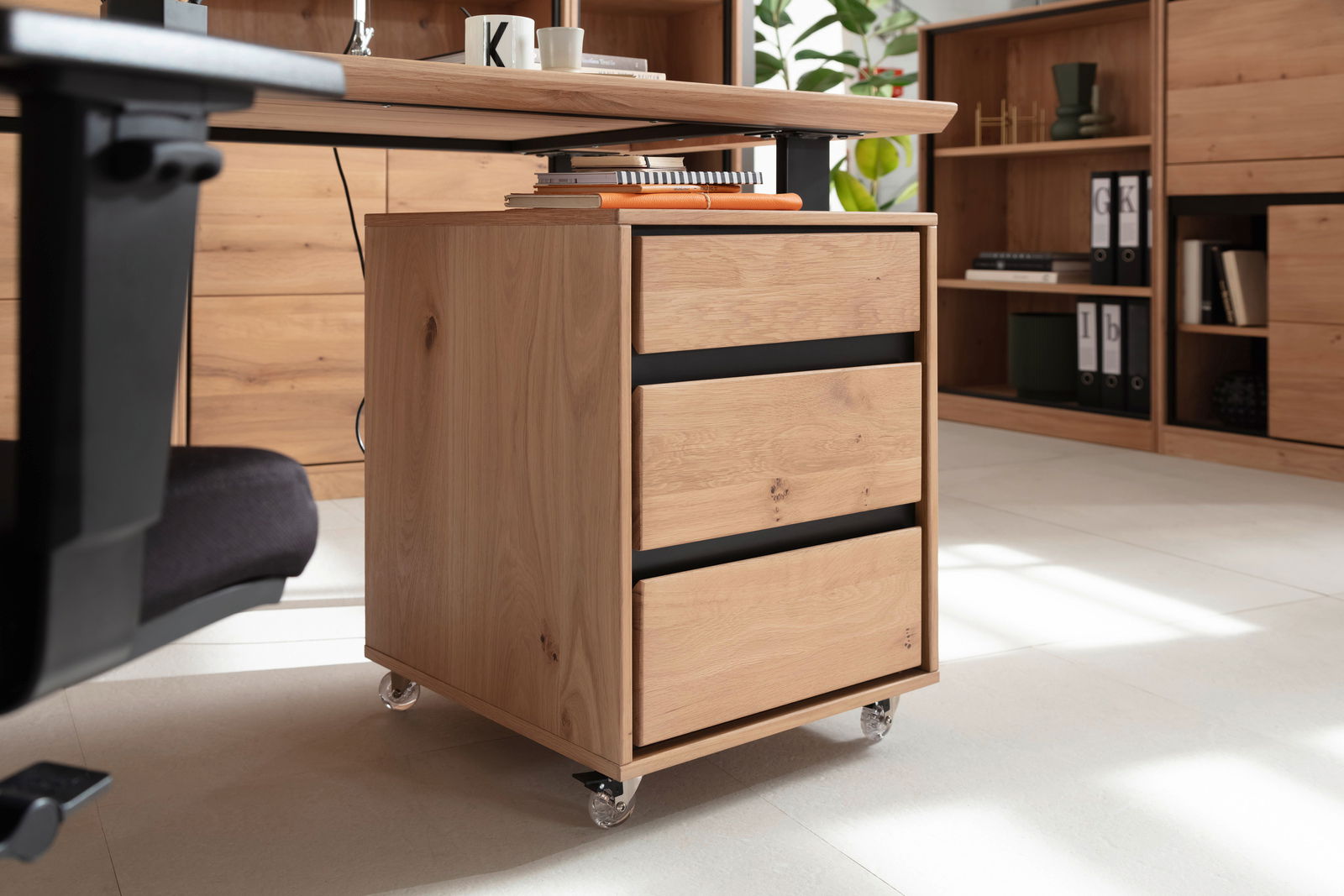 Rollcontainer aus Holz mit drei Schubladen, auf Rollen, seitliche Perspektive unter einem Schreibtisch.