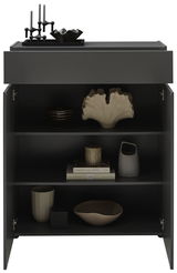 Schwarze Kommode mit geöffneter Tür, dekoriert mit Kerzenhaltern und Schalen auf der Oberseite, und verschiedenen Dekorationsobjekten sowie Büchern in den Regalfächern, frontal betrachtet.