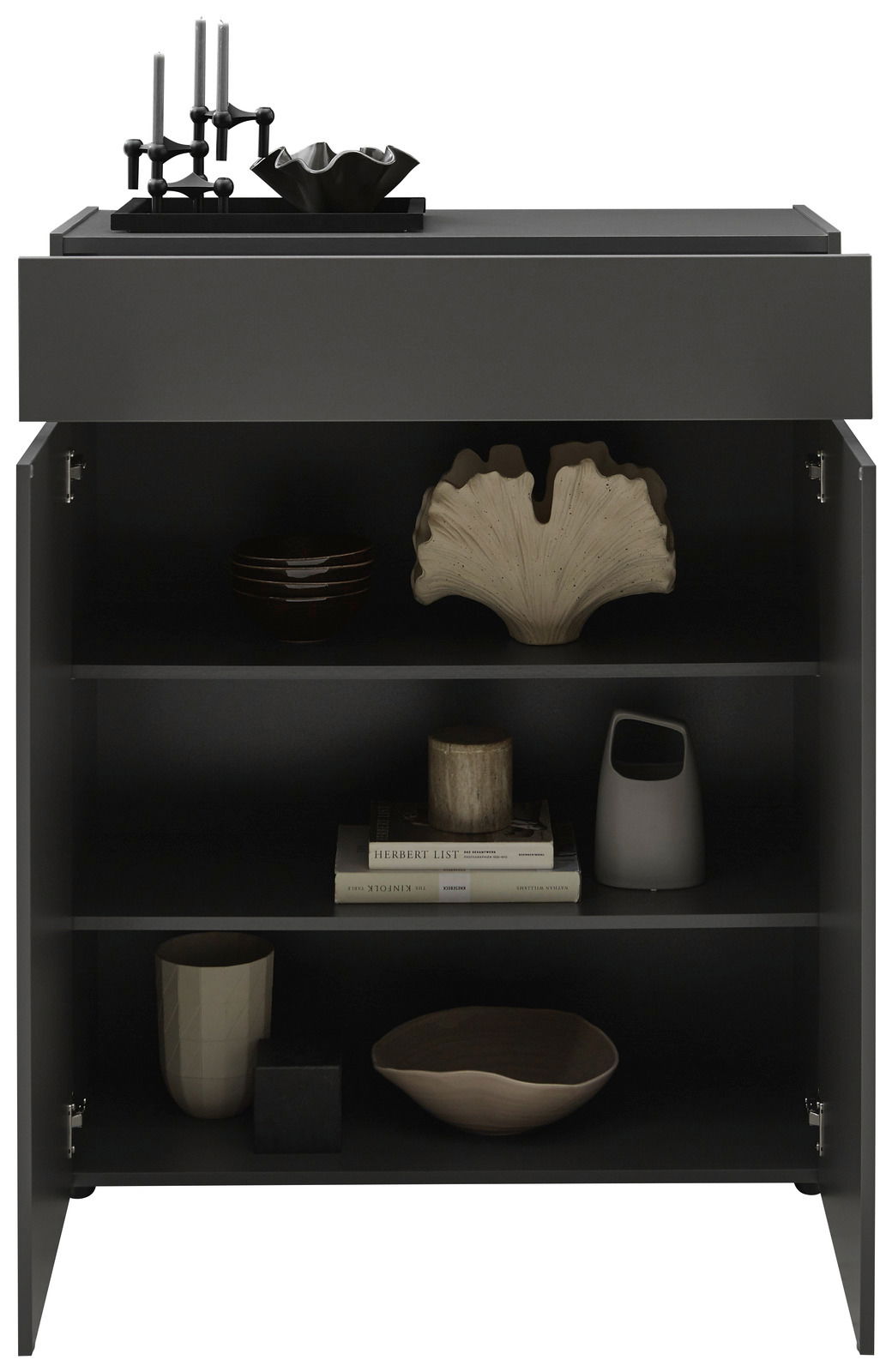 Schwarze Kommode mit geöffneter Tür, dekoriert mit Kerzenhaltern und Schalen auf der Oberseite, und verschiedenen Dekorationsobjekten sowie Büchern in den Regalfächern, frontal betrachtet.