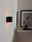Moderne schwarze Wandleuchte XERA von Lucide, seitliche Perspektive, beleuchtet eine weiße Wand mit warmem Licht.