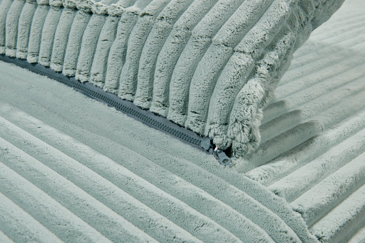 Nahaufnahme eines hellgrünen Funktionssofas mit weichem, geripptem Stoff und sichtbarem Reißverschluss.