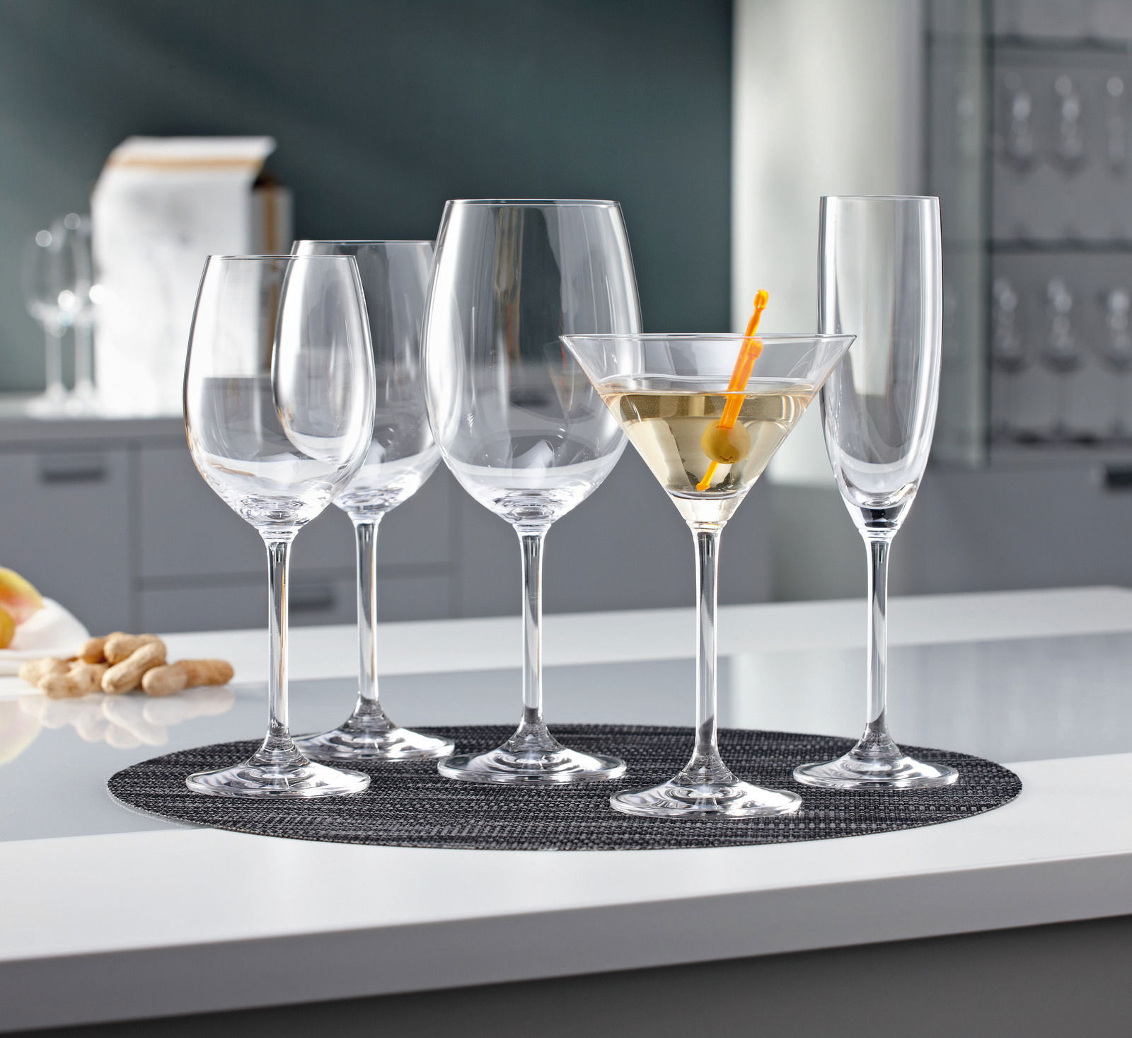 Leonardo Cocktailglas Daily Eine Auswahl an eleganten Gläsern, darunter ein Cocktailglas mit einem Getränk und einer Olive, auf einem Tisch aus der Seitenperspektive fotografiert.