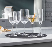 Eine Auswahl an eleganten Gläsern, darunter ein Cocktailglas mit einem Getränk und einer Olive, auf einem Tisch aus der Seitenperspektive fotografiert.