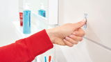 Hand drückt tesa Powerstrip an eine weiße Wand im Badezimmer, seitliche Perspektive