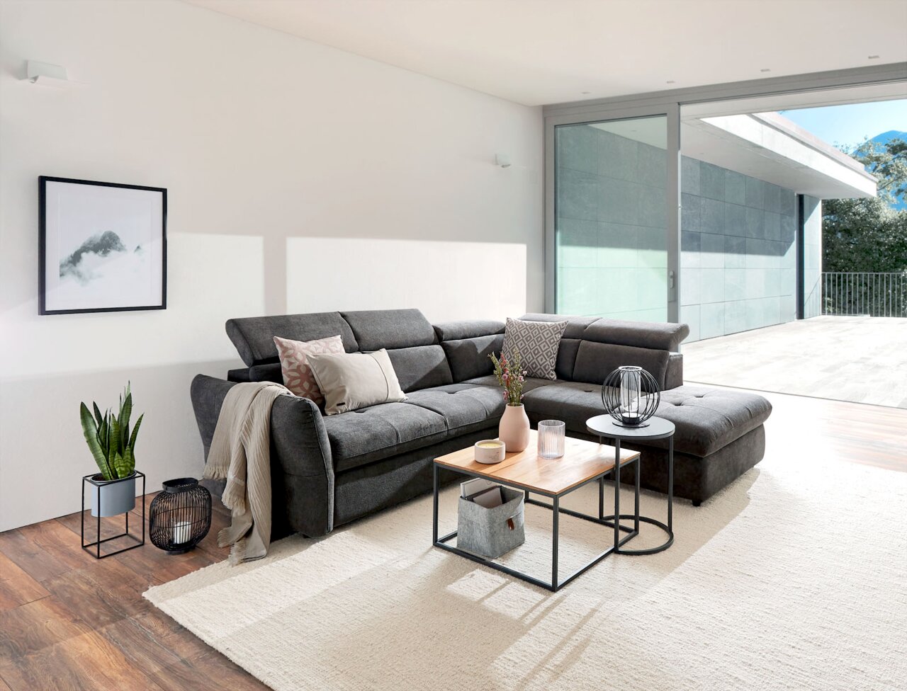 Moderner Beistelltisch in einem hellen Wohnzimmer, frontal fotografiert, neben einer grauen Polsterecke mit dekorativen Kissen.