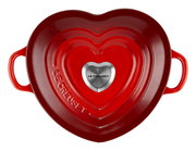 Herzförmiger, kirschroter Bräter von oben mit zwei Griffen und einem silbernen Knauf in der Mitte, Le Creuset-Logo sichtbar.