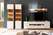 Wohnzimmer-Wohnwand in Weiß und Holzoptik mit zwei beleuchteten Vitrinen, TV-Lowboard und Wandboard vor dunkelgrauer Wand, frontal aus Augenhöhe fotografiert