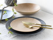 Ein elegantes Tellerset bestehend aus einem 18-teiligen Set mit modernen, geriffelten Tellern in verschiedenen Farben, präsentiert auf einem Tisch mit goldfarbenem Besteck. Perspektive von schräg oben.