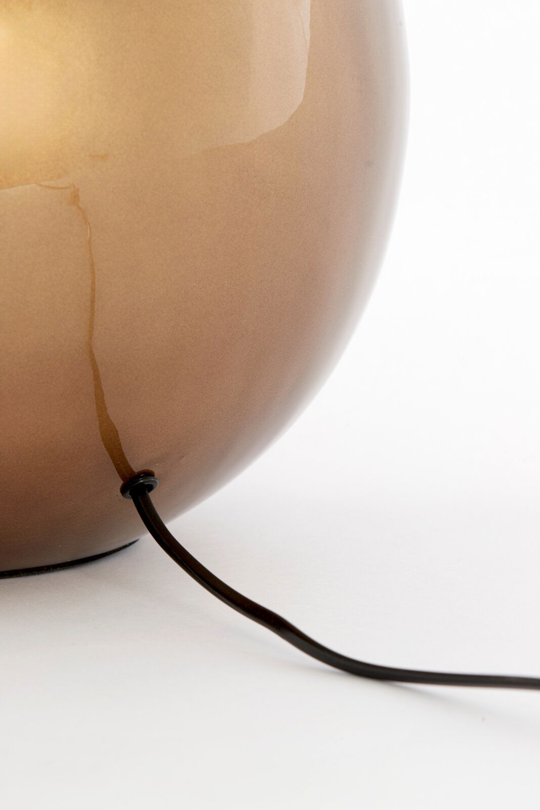 Nahaufnahme eines runden, glänzenden Lampenfußes in Braun mit einem schwarzen Kabel, das aus der unteren Seite herausführt.