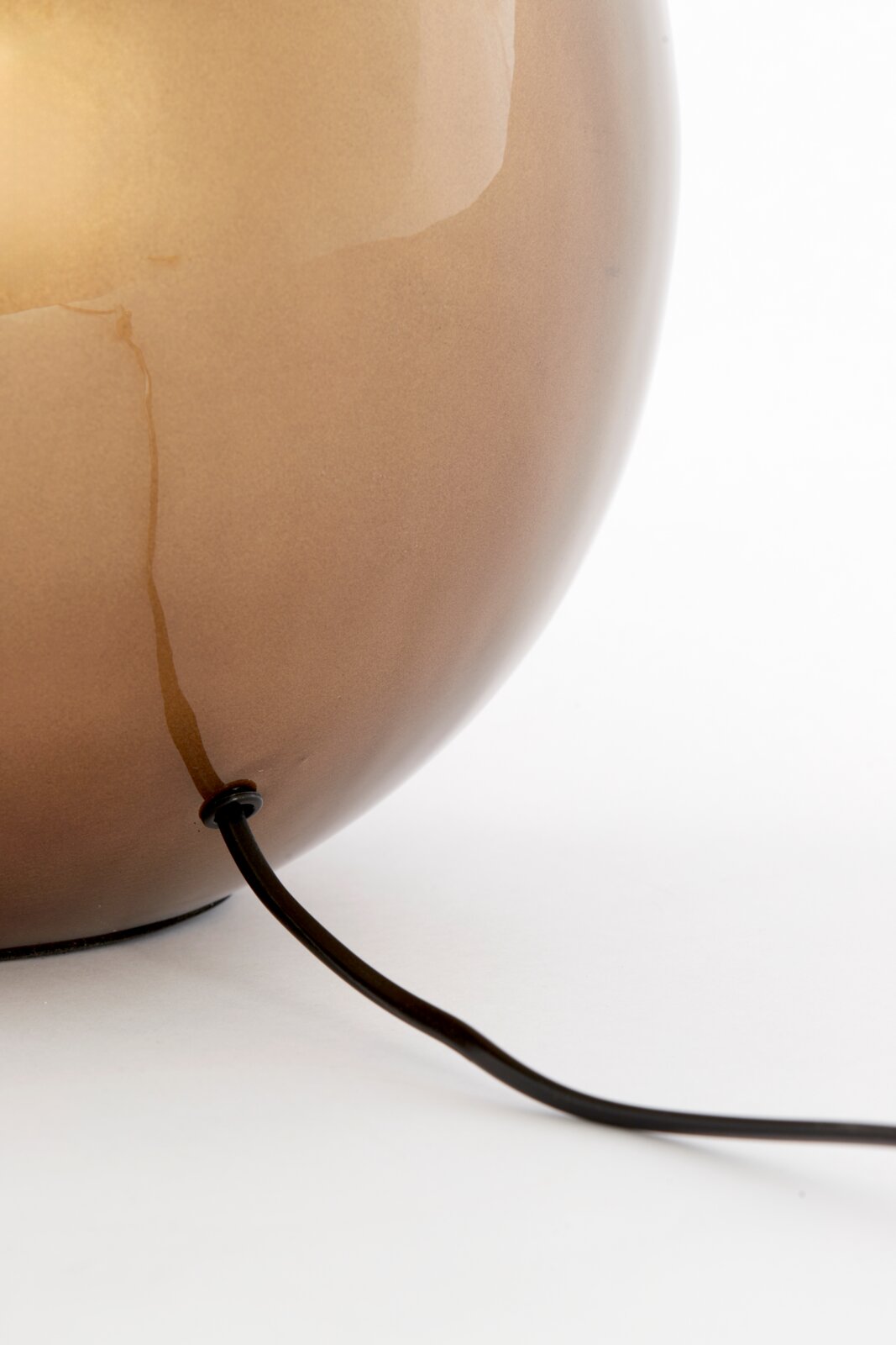 Close-up van een ronde, glanzende lampvoet in bruin met een zwarte kabel die aan de onderkant naar buiten loopt.