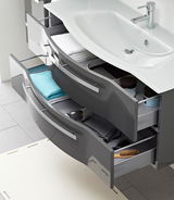 Moderner Badblock mit geschwungenem Waschbecken und zwei offenen Schubladen, gefüllt mit Handtüchern und Pflegeprodukten, aus der Vogelperspektive.