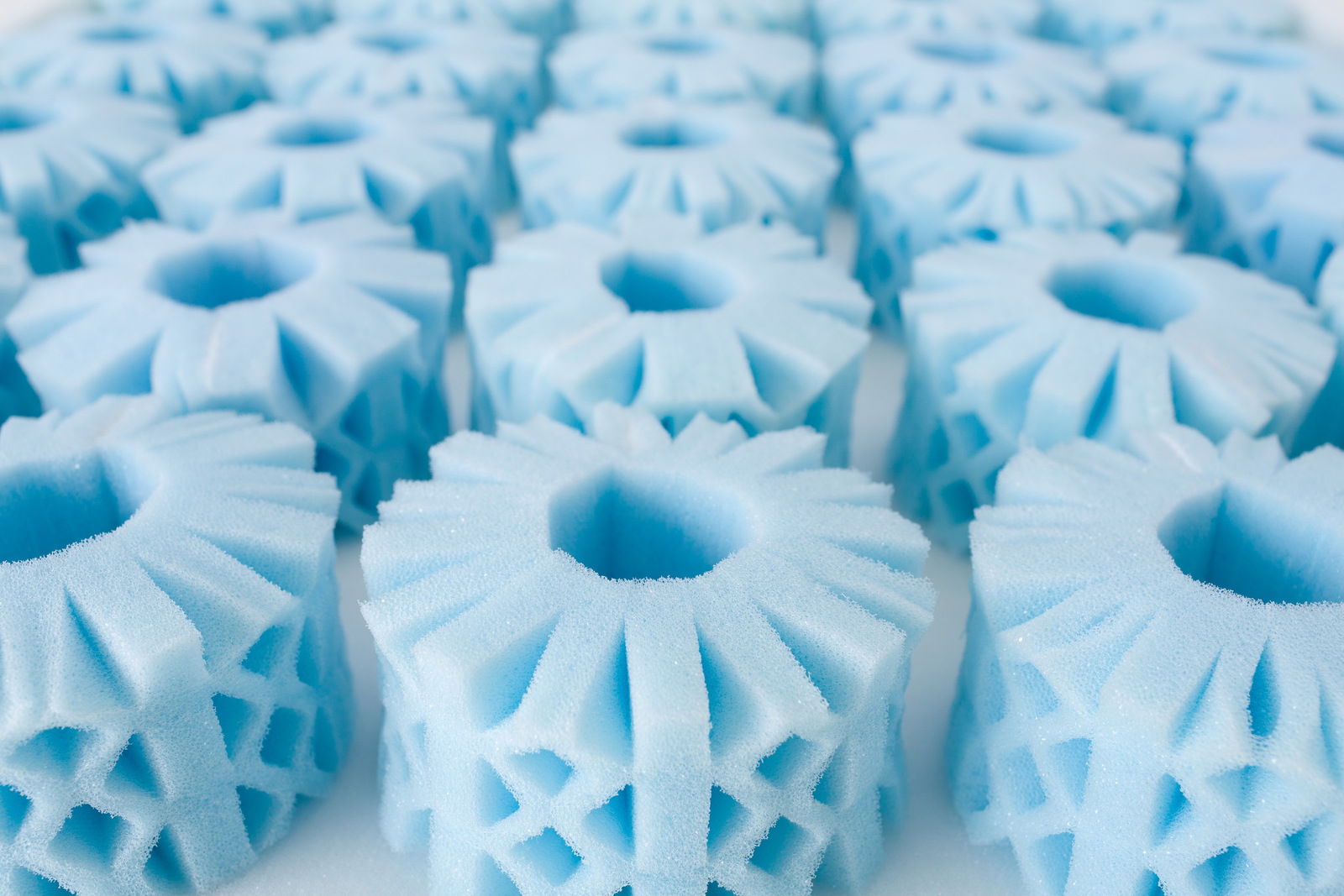 Nahaufnahme von blauen Schaumstoffelementen mit sechseckigen Öffnungen, die in einer Reihe angeordnet sind, aus einer seitlichen Perspektive.