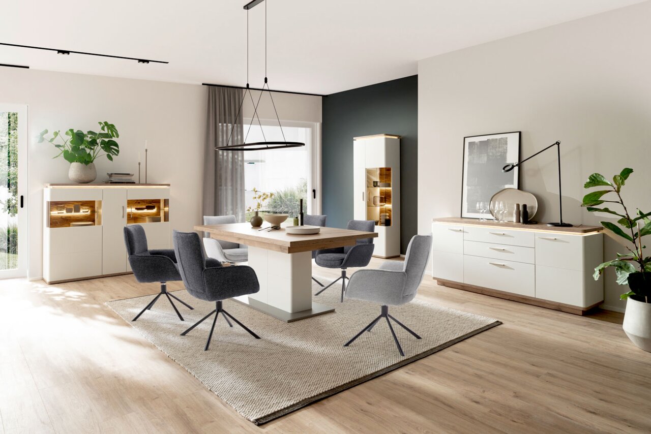 Novel Armlehnstuhl ISABEL Modernes Esszimmer-Set mit weißer Anrichte und Vitrine mit Holz-Akzenten und LED-Beleuchtung, großem Esstisch und grauen Polsterstühlen auf Teppich, aufgenommen in leichter Schrägansicht von vorn.