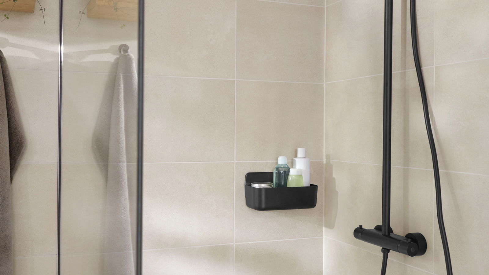 Tesa Duschkorb LAVAA Schwarzer Duschkorb von tesa Lavaa, montiert an einer beigen Badezimmerwand, gefüllt mit Duschutensilien, seitliche Perspektive.