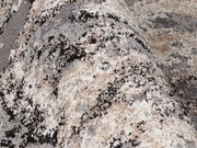 Nahaufnahme eines Designer-Teppichs Juwel Liray mit abstraktem Muster in Grau-, Beige- und Schwarztönen, perspektivisch von der Seite aufgenommen.