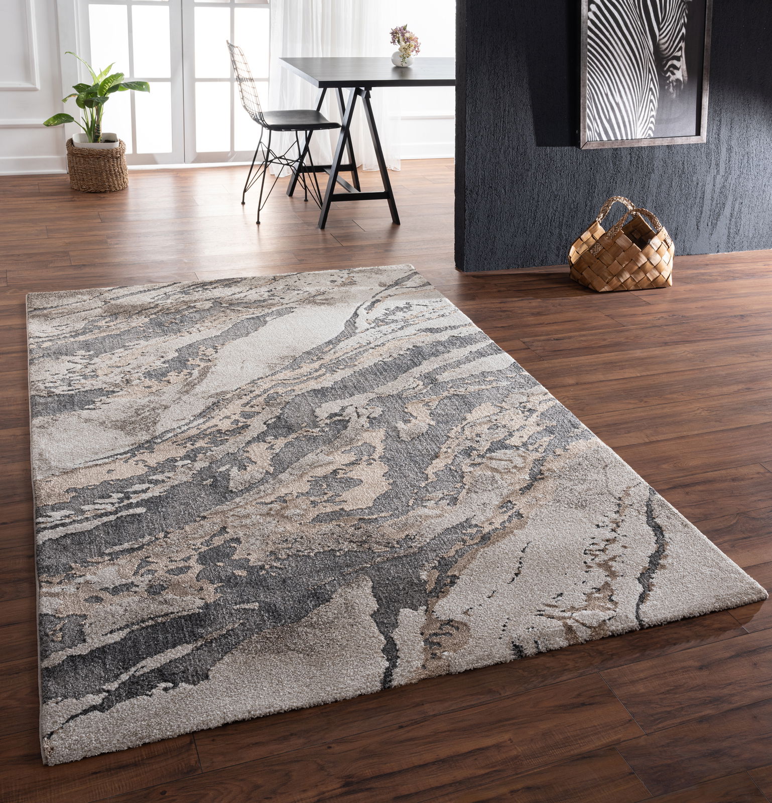 Moderner Teppich mit abstraktem Muster in Grau- und Beigetönen, auf einem Holzboden in einem stilvoll eingerichteten Raum. Perspektive von schräg oben.