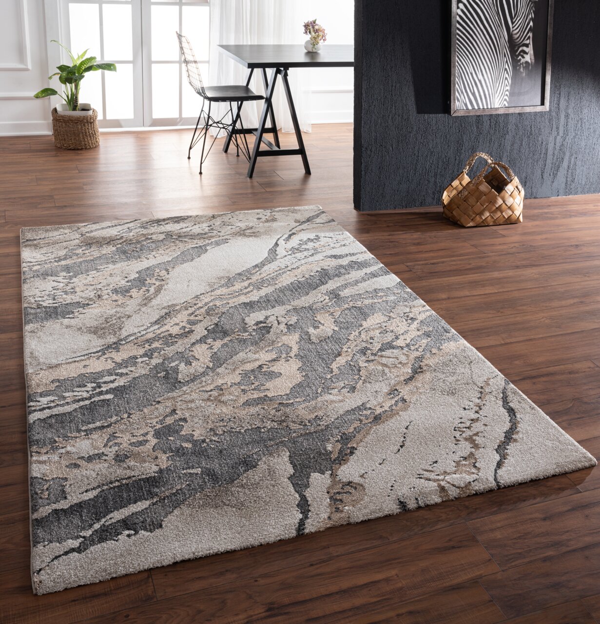 Merinos Webteppich MARVELLOUS Moderner Teppich mit abstraktem Muster in Grau- und Beigetönen, auf einem Holzboden in einem stilvoll eingerichteten Raum. Perspektive von schräg oben.