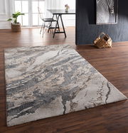 Moderner Teppich mit abstraktem Muster in Grau- und Beigetönen, auf einem Holzboden in einem stilvoll eingerichteten Raum. Perspektive von schräg oben.