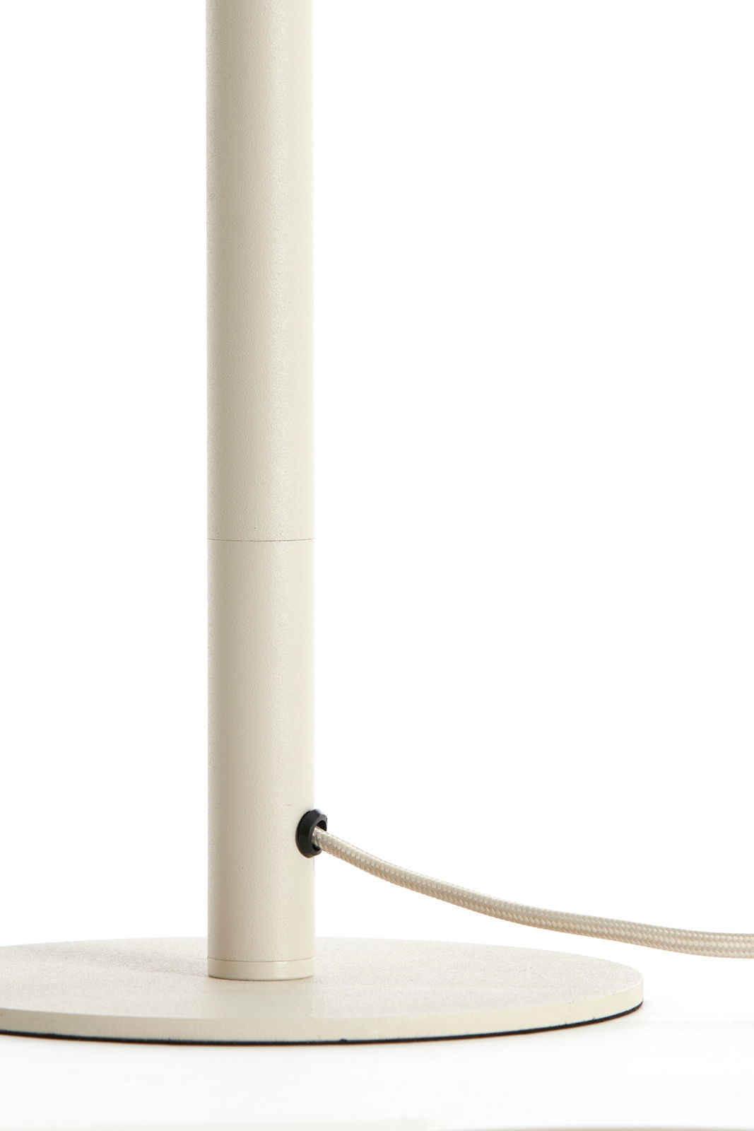 Nahaufnahme eines cremefarbenen Lampenfußes mit rundem Sockel und einem Kabel, das seitlich herausführt.
