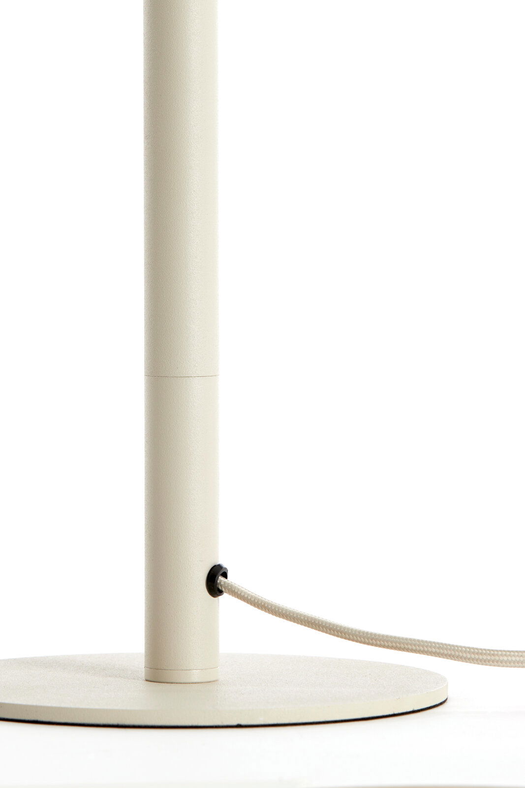 Nahaufnahme eines cremefarbenen Lampenfußes mit rundem Sockel und einem Kabel, das seitlich herausführt.