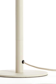 Nahaufnahme eines cremefarbenen Lampenfußes mit rundem Sockel und einem Kabel, das seitlich herausführt.