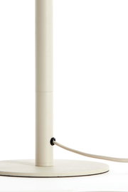Close-up van een crèmekleurige lampvoet met een ronde voet en een kabel die aan de zijkant naar buiten loopt.