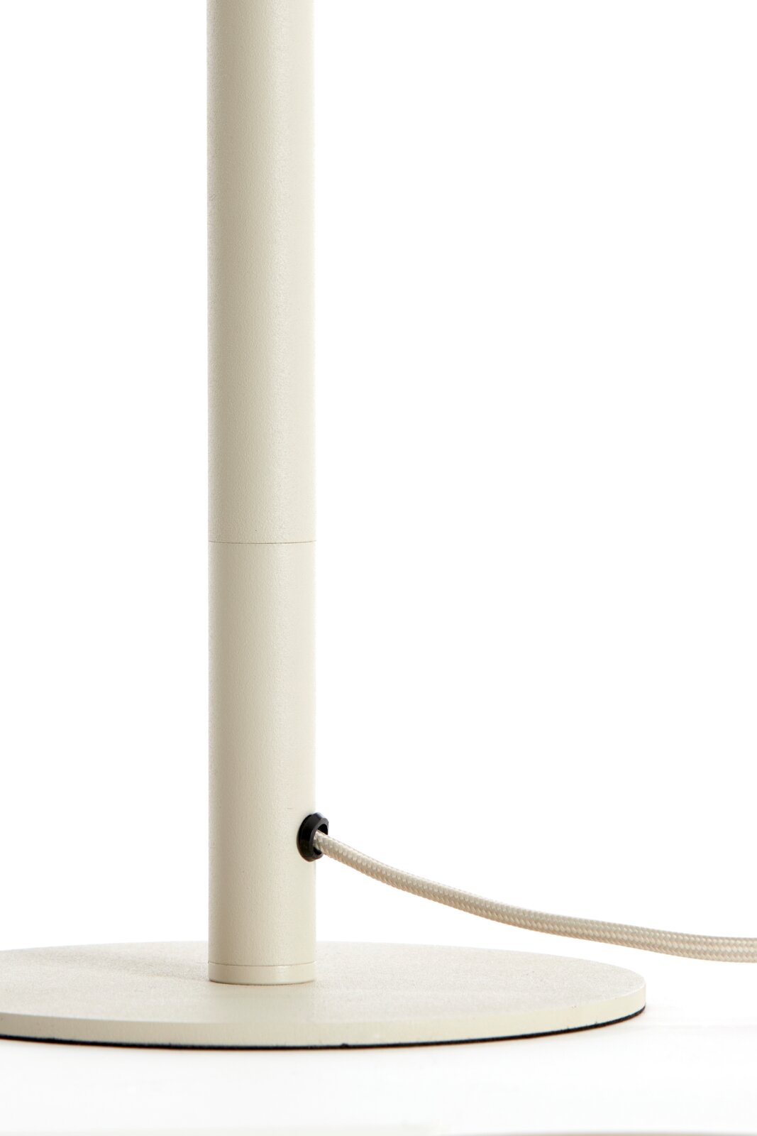 Close-up van een crèmekleurige lampvoet met een ronde voet en een kabel die aan de zijkant naar buiten loopt.
