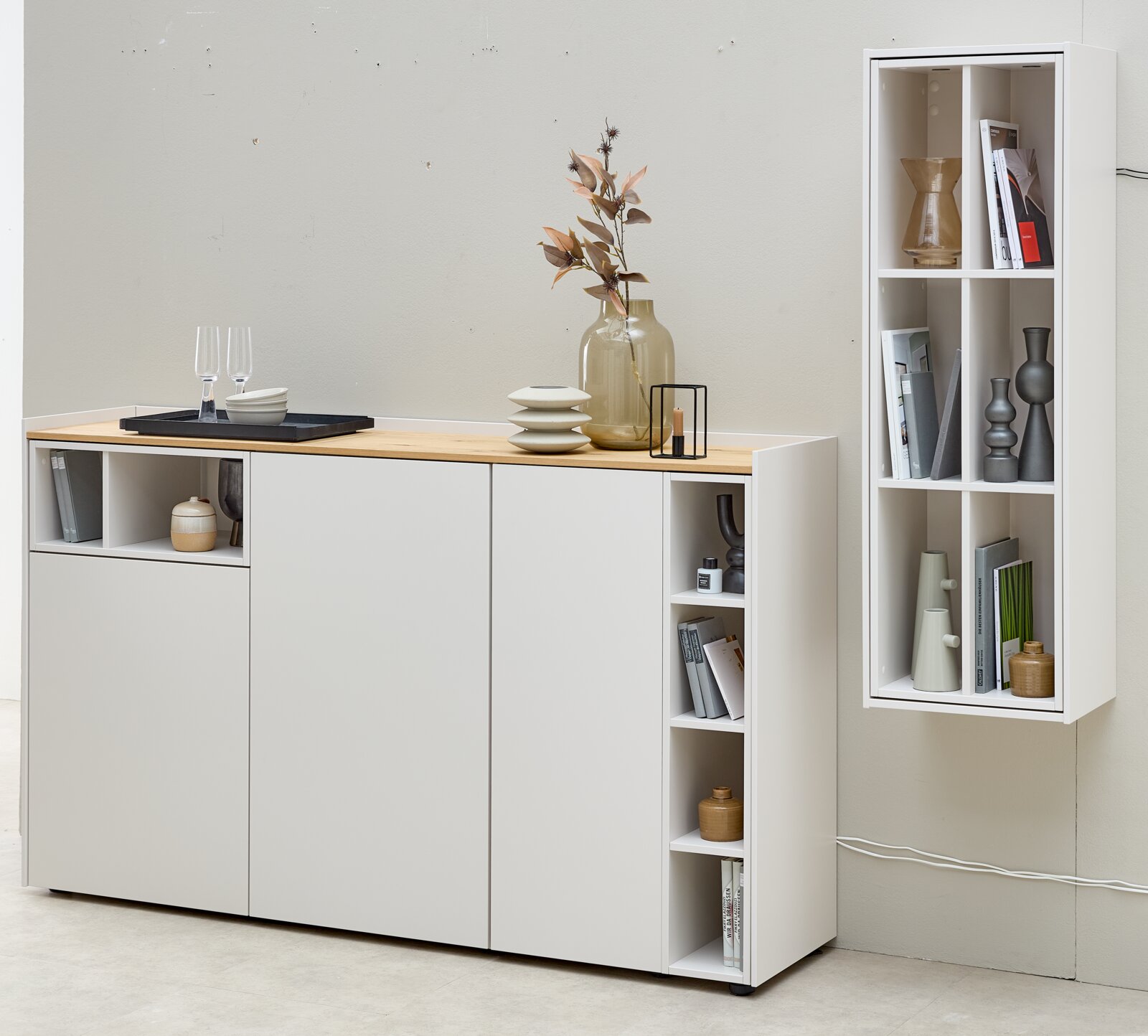 Vooraanzicht van een moderne witte opbergkast met deuren, open vakken en een naturel houten blad, gecombineerd met een hoge wandkast met open vakken.