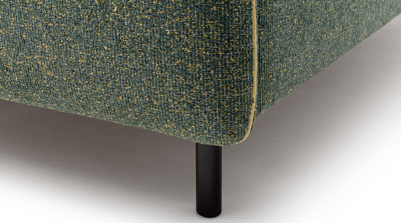 Close-up van een gestoffeerd bed met groene bekleding en zwarte metalen poten, gezien vanaf de zijkant