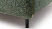 Close-up van een gestoffeerd bed met groene bekleding en zwarte metalen poten, gezien vanaf de zijkant