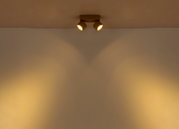Zweiflammiger Deckenstrahler in Weiß mit warmem Lichtkegel an der Wand, fotografiert in Frontalansicht leicht von unten