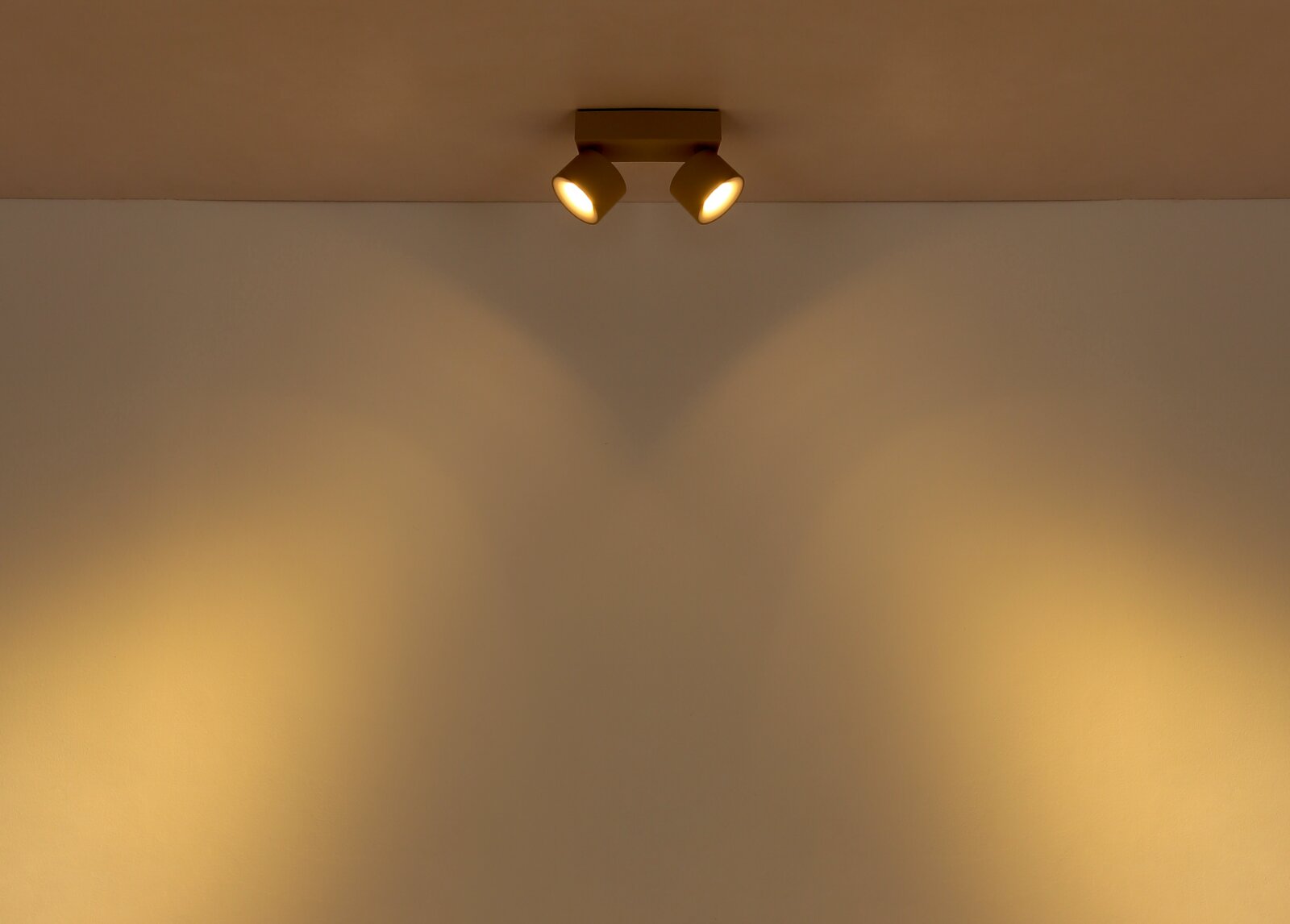 Zweiflammiger Deckenstrahler in Weiß mit warmem Lichtkegel an der Wand, fotografiert in Frontalansicht leicht von unten