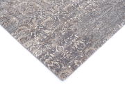 Nahaufnahme eines Designer-Teppichs mit abstraktem Muster in Grau- und Beigetönen, perspektivisch von der Ecke aufgenommen.