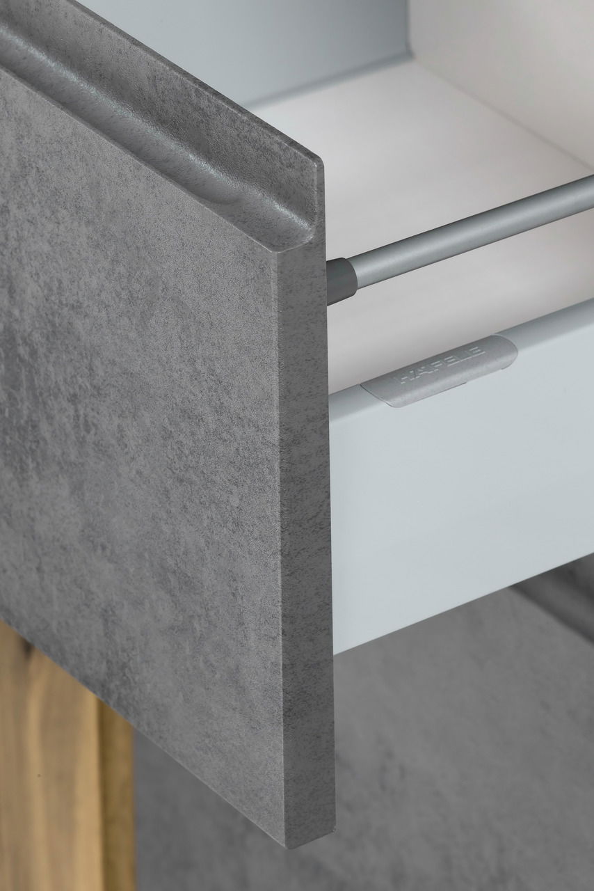 Nahaufnahme einer Schublade mit grauer, steinartiger Front und Metallgriff, perspektivisch von der Seite aufgenommen.