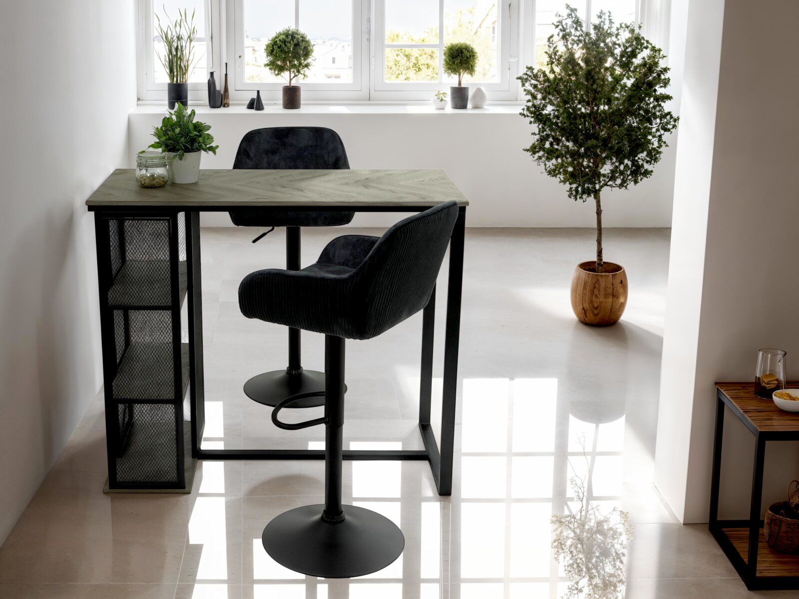 Z2 Bar KLARA Moderne bartafel met een zwart metalen onderstel en een groenachtig tafelblad, met planken aan de zijkanten, omringd door planten, gezien vanuit een lichte ruimte met grote ramen.