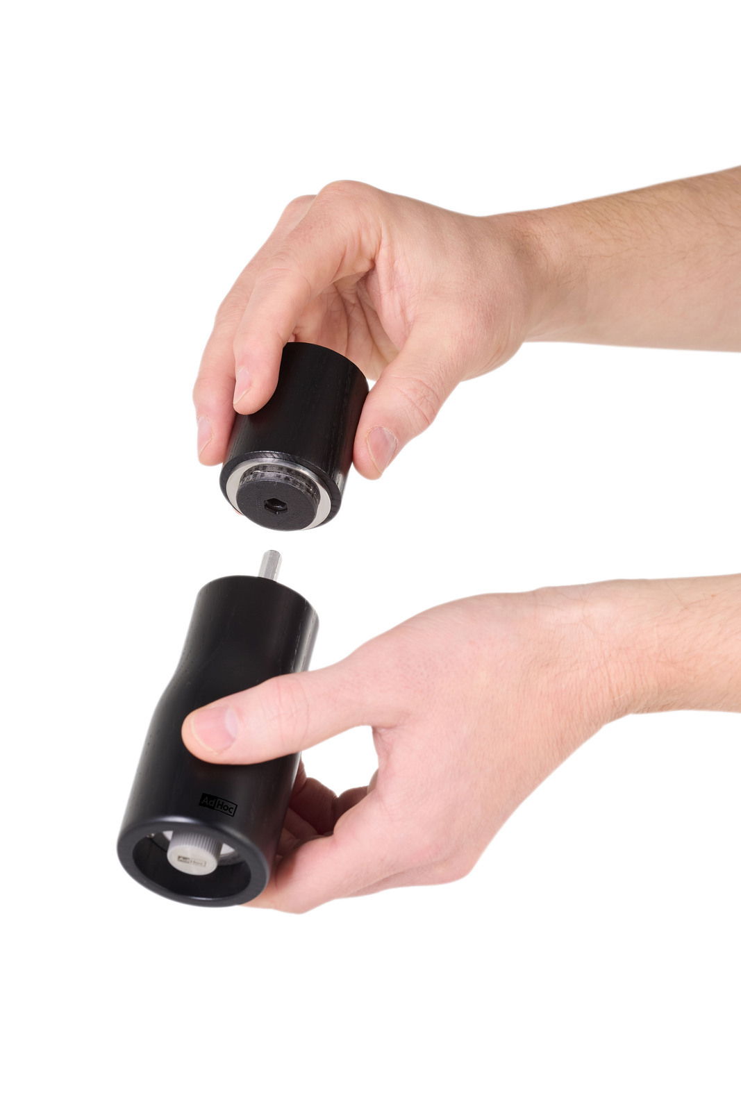 Zwei Hände halten eine schwarze Pfeffer- oder Salzmühle, die in zwei Teile zerlegt ist. Die Perspektive zeigt die Mühle von der Seite.