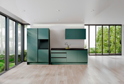 Moderne grüne Küchenzeile mit Schränken und Arbeitsplatte, frontal betrachtet, in einem hellen Raum mit großen Fenstern.