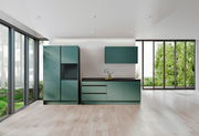 Moderne grüne Küchenzeile mit Schränken und Arbeitsplatte, frontal betrachtet, in einem hellen Raum mit großen Fenstern.