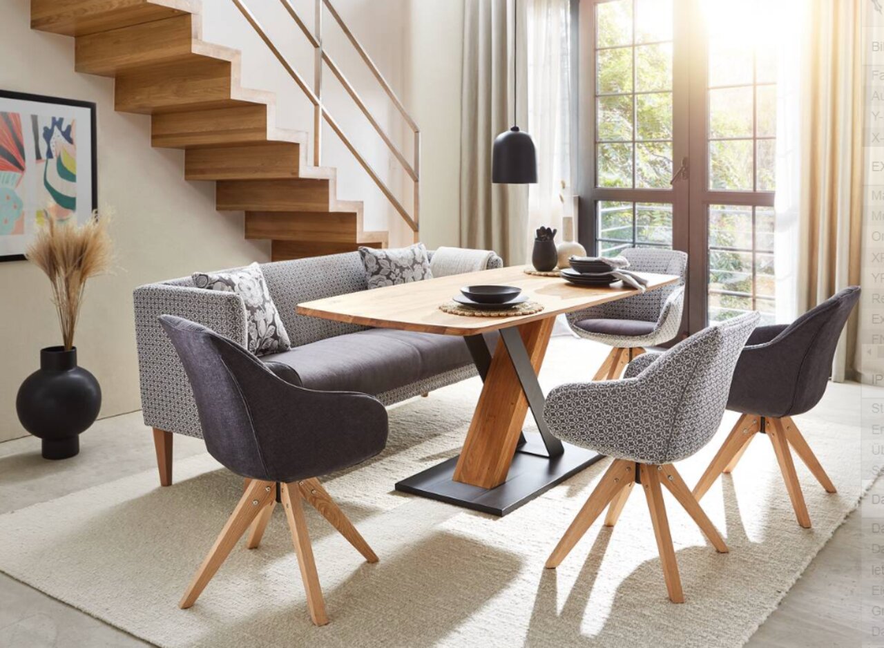 Moderner Esstisch mit Holzplatte und Metallgestell, umgeben von stilvollen Stühlen und einer Couch, in einem hellen Raum mit Treppe und großen Fenstern, seitliche Perspektive.