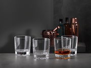 Vier Whiskygläser in einem modernen, eleganten Design, eines davon mit Whisky gefüllt, auf einer grauen Oberfläche mit einer stilvollen Bar im Hintergrund, seitliche Perspektive.