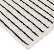 Nahaufnahme einer cremefarbenen Badematte mit schwarzen Streifen, diagonale Perspektive auf die Ecke.