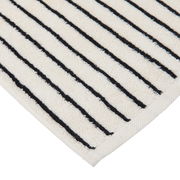 Nahaufnahme einer cremefarbenen Badematte mit schwarzen Streifen, diagonale Perspektive auf die Ecke.