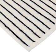 Close-up van een crèmekleurige badmat met zwarte strepen, diagonaal perspectief op de hoek.